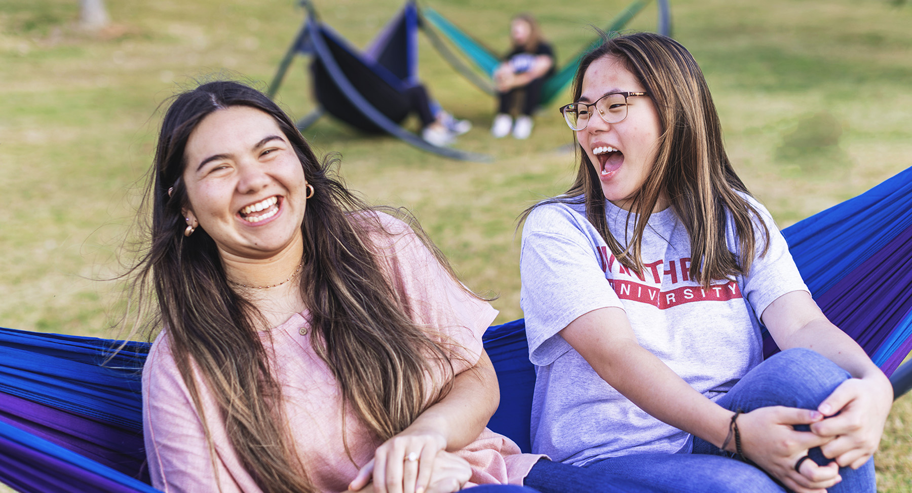 Two girls sit together laughing in a hammock outdoors