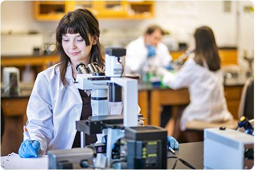 Student in a lab coat using a microscope