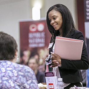 a girl in business attire holding a folder and talking to someone at a event