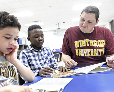 a student teacher sits with two young children reading together.