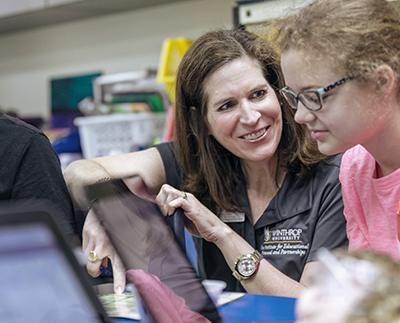 A teacher smiles at a middle school student working on a lesson.