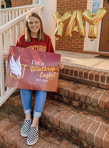 a smiling student next to a YAY balloon holding a sign that says I'm a Winthrop Eagle