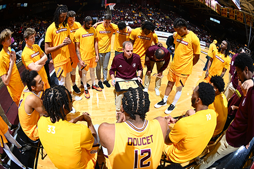 Men's Basketball team huddled around Coach Mark Prosser during a game