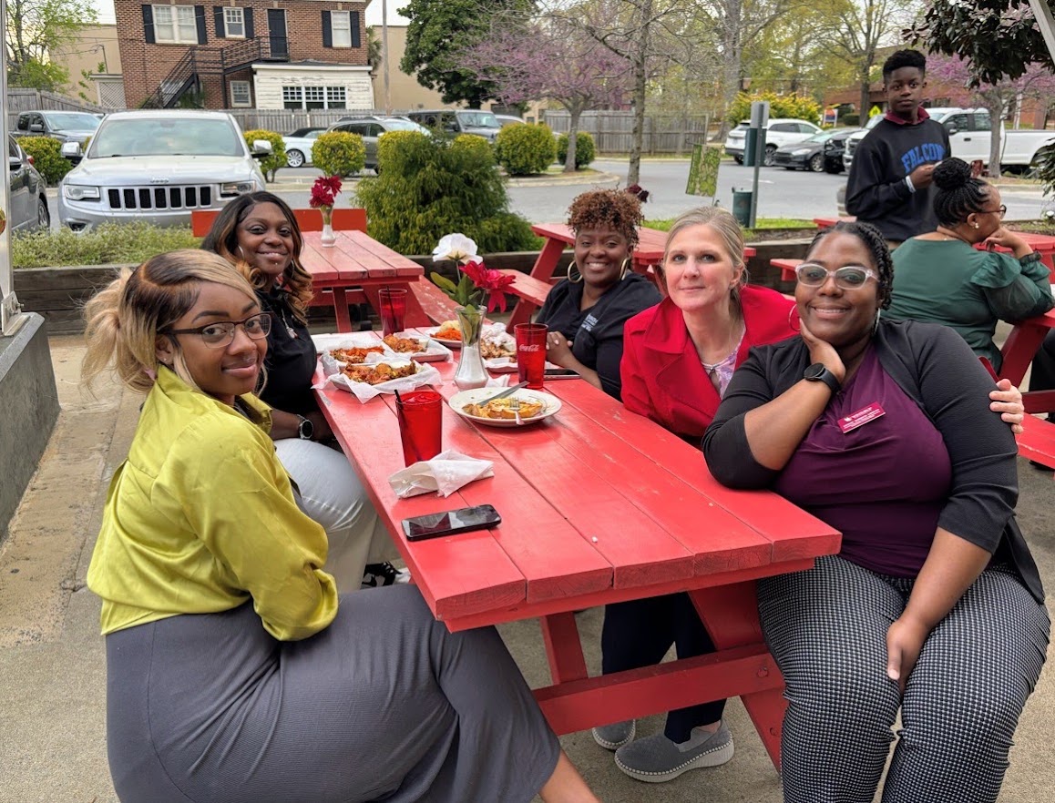 A group photo of Social Work students sitting around a red table for lunch
