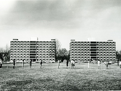 Archery targets are set along the grass in front of two eight-story tall buildings.
                     Black and white