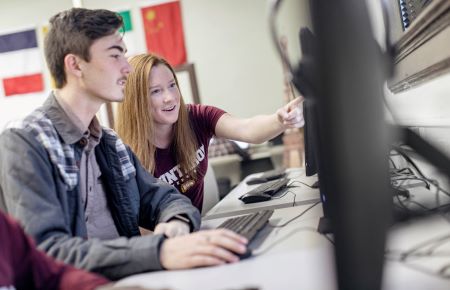 Student helping student at a computer.