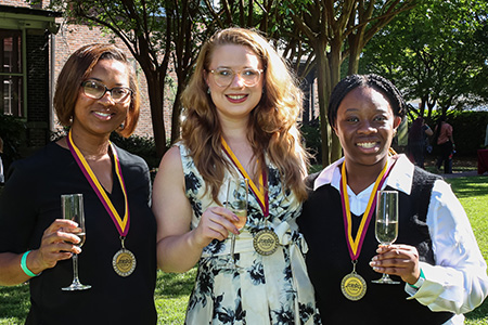 thee students wearing medals and holding up glasses of champagne
