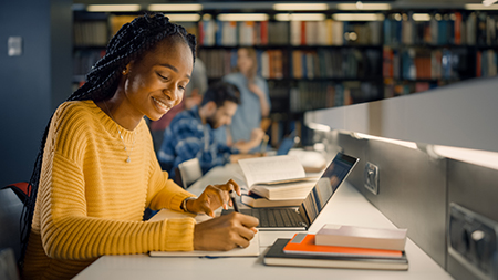 Student working in the library with a notepad and laptop