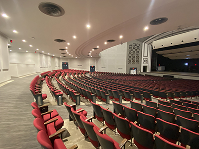 Red auditorium seats; white ceiling; bright lights facing a stage