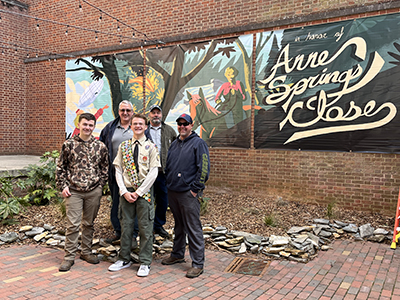 Five men standing in a brick courtyard in front of a sign reading 'Anne Springs Close'