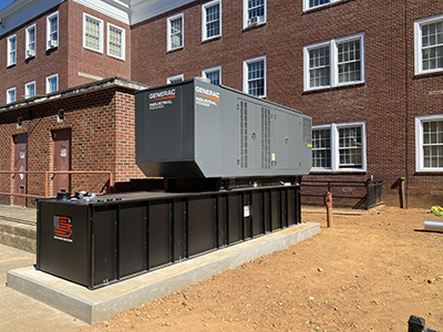 Mechanical generator sitting on concrete platform behind brick building