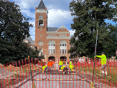 View of a brick clock tower building (Tillman Hall) with a construction crew pouring
                        concrete