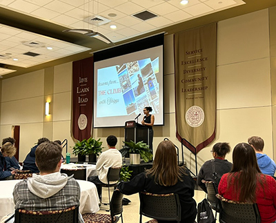a speaker standing at a lectern in richardson ballroom on the winthrop university
                        campus. she is speaking to a crowded room