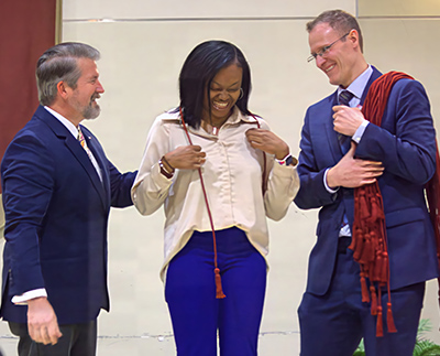 a smiling honors student being corded by the provost and dean of the honors college