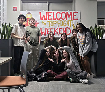 Group photo of current Honors Top Flight Ambassadors posing in front of handmade Welcome
                        weekend sign