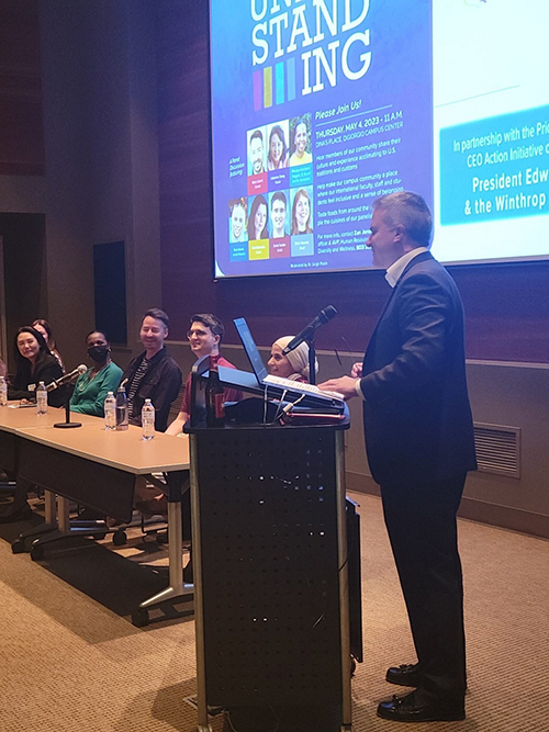 Winthrop President Edward Serna speaks at a podium beside the table of panelists at
                        the 2023 Day of Understanding event