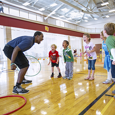 PE student playing with elementary school kids in the gym