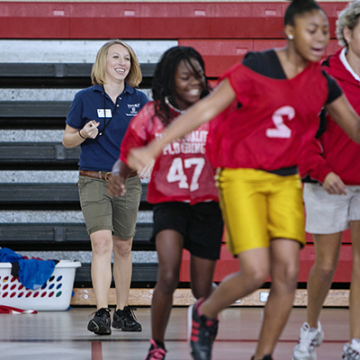 PE teacher smiling behind kids playing in a school gym