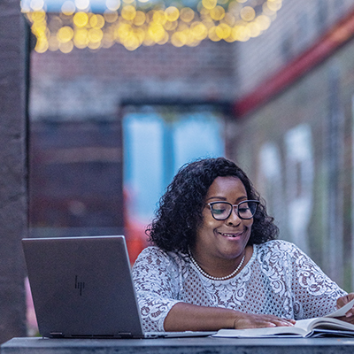 Smiling woman reading a textbook next to a laptop