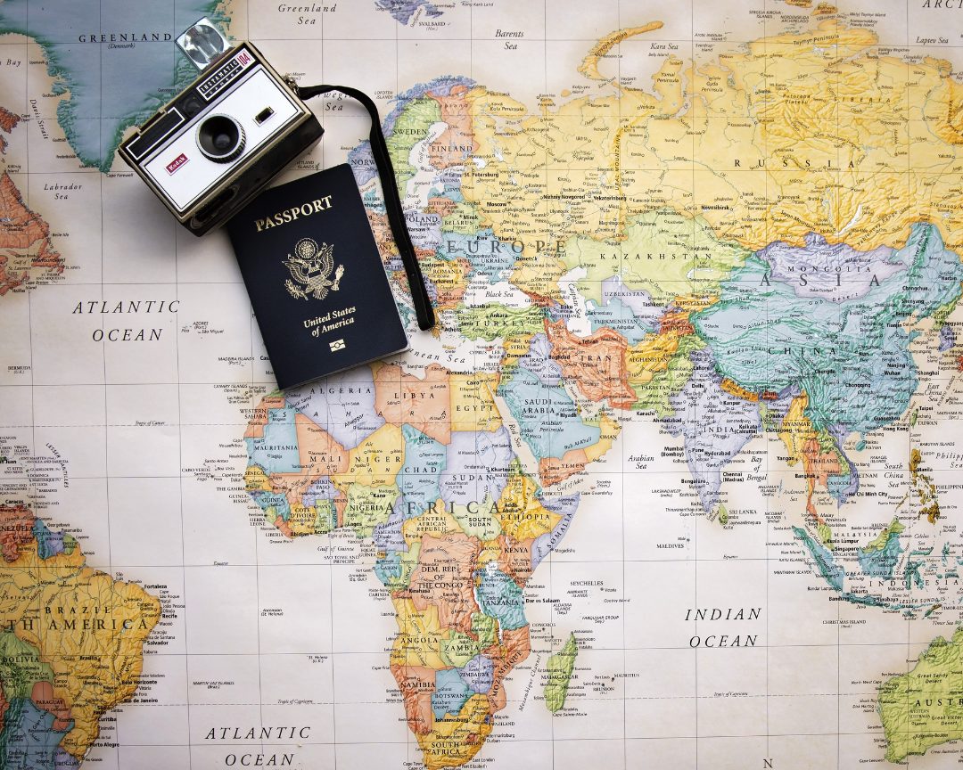 A passport and vintage camera sit on top of a world map in various colors