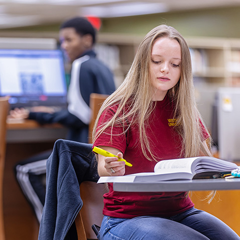 a student holding a highlighter while reading a textbook