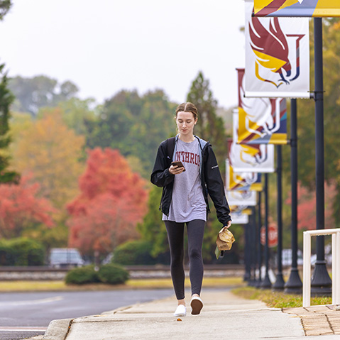 a student walking down the sidewalk looking at her phone