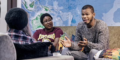 three students talking in front of a large world map