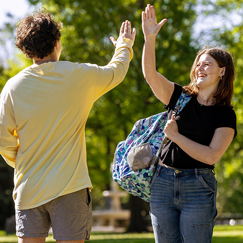 two students high-fiving outside on campus