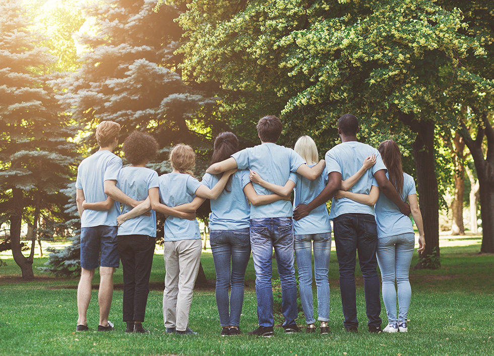 Group Photo a group of people standing facing away from the camera with their arms around each
other. The people are different ages, genders and ethnicities, and they are wearing
matching light blue shirts