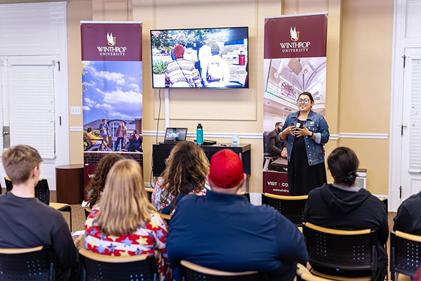 an admissions counselor speaking to a room full of prospective students and their
                  families