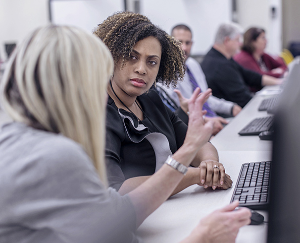 two women having a classroom discussion with other adult students visible in the background
                        during a continuing professional education class