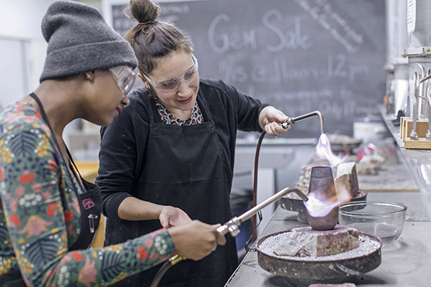 an art professor showing a student how to use a blow torch in the metal studio