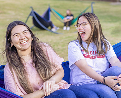 two students sitting in a hammock on a sunny day and laughing
