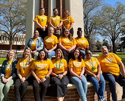a group photo of Winthrop admissions staff sitting around the base of the eagle statue
                        on a sunny day