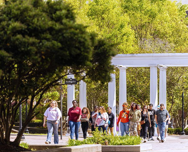 an admissions ambassador leading a group of prospective students and their families
                        on a tour of campus. They are walking through Hardin Gardens on a sunny day with everything
                        in bloom