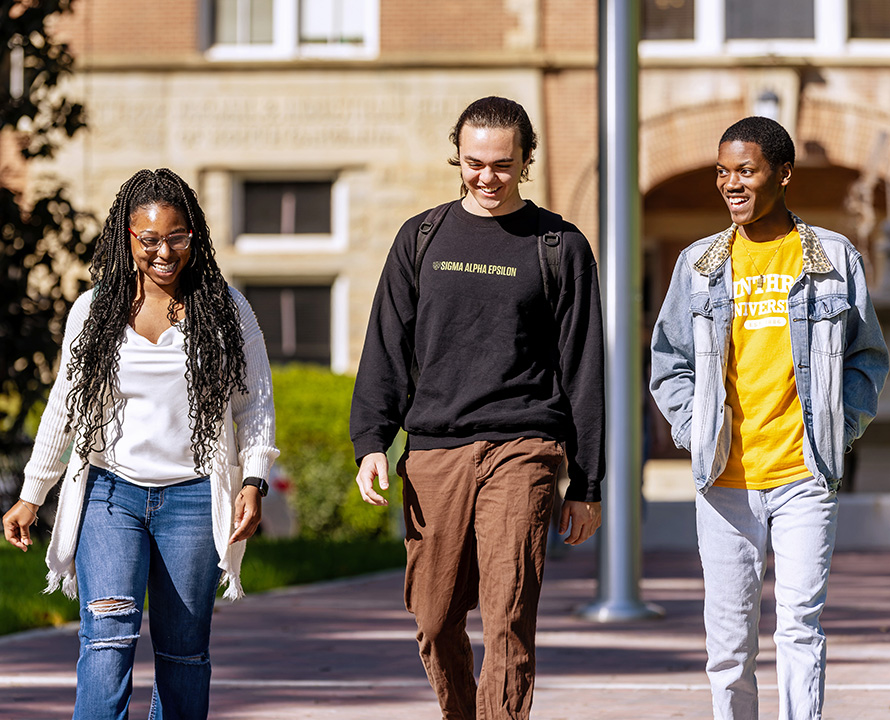 three smiling students walking on campus