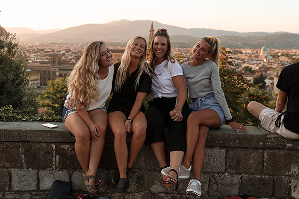 four students sitting together in Italy with a city visible behind them