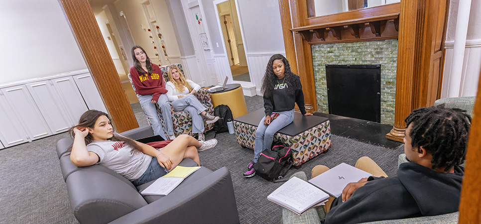 a group of students studying near a fireplace in the lobby of their dorm