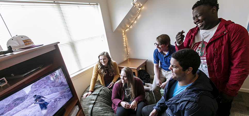 a group of students playing video games in a dorm lounge