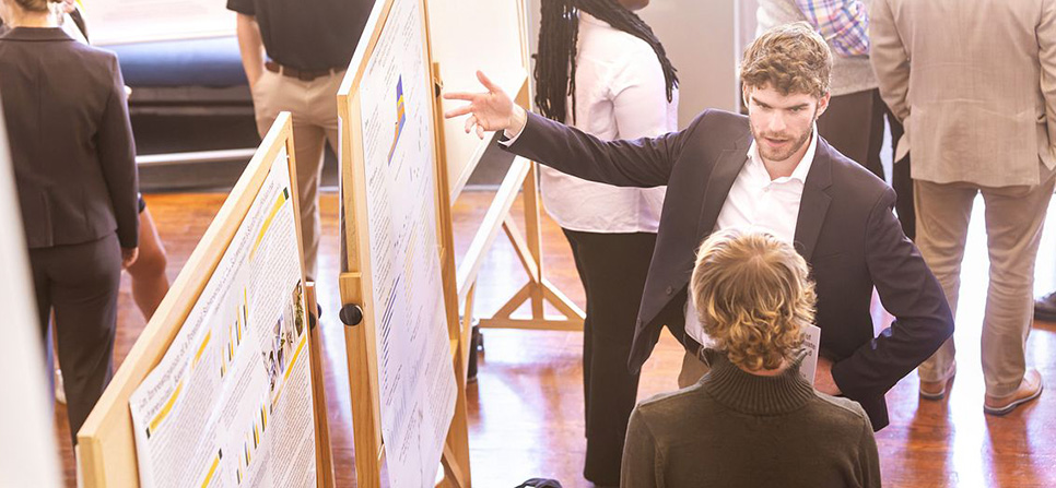 a student giving a poster presentation wearing a suit