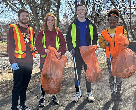 four students in high vis vests picking up litter
