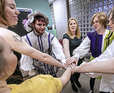 a group of theatre students in costume putting their hands together in a circle before
                              heading out on stage