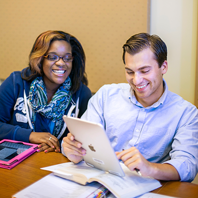 Woman and man looking at an iPod while sitting at a desk covered in books