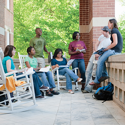 Groups of people sitting on a porch in rocking chairs holding books