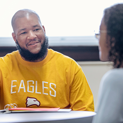 African American man sitting at a table with a binder talking to a student