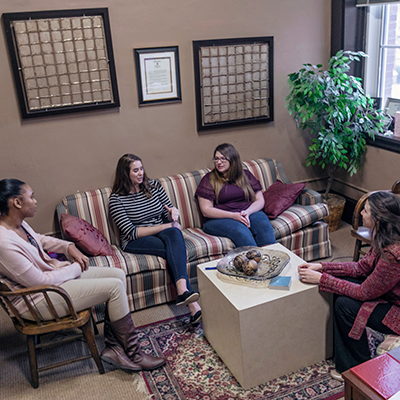 Group of four people sitting on a couch and chairs while talking