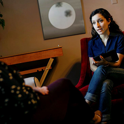 Photo of a woman in a dim room leaning over a tablet and talking to a person who is
                           mostly off-screen