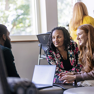 Three people talking while sitting around a laptop