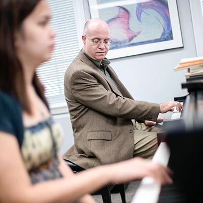 Male teacher in a tan blazer teaching a student to play piano