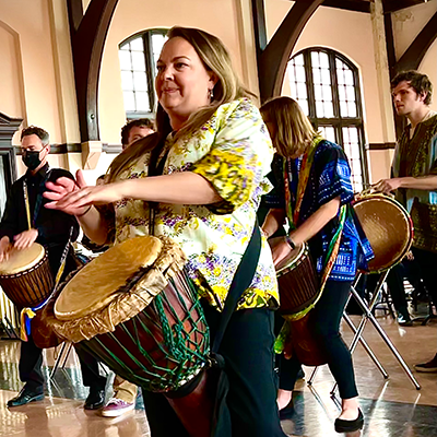 Woman playing a large drum with her hands while other people play drums in the background